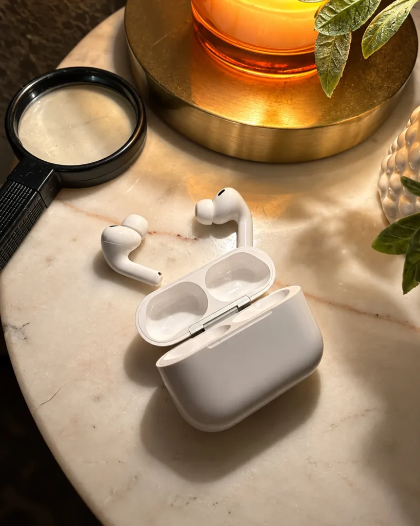 AirPods Pro 3 earbuds beside their open charging case on a marble tabletop.